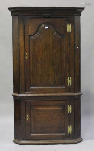 A George III provincial oak floor standing corner cabinet, the moulded pediment above two panelled