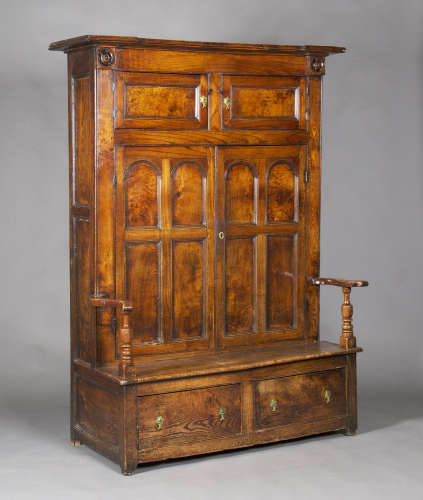 An 18th century provincial elm and ash bacon cupboard settle, the overhanging pediment above a