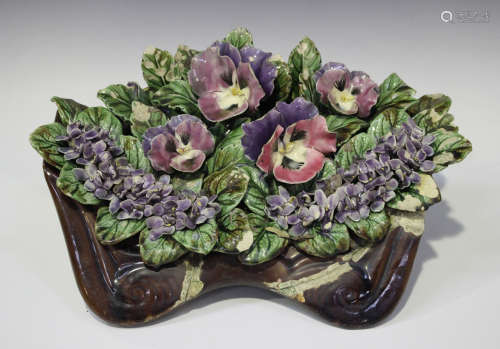 A pottery display of flowers in a brown glazed trough, probably French circa 1900, including pansies