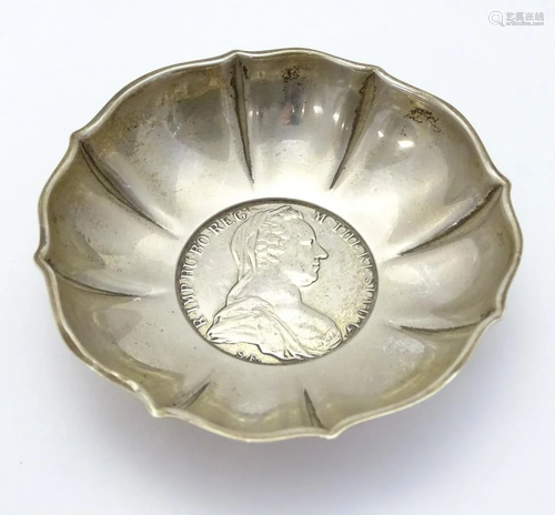 A small white metal dish with inset Austrian coin to