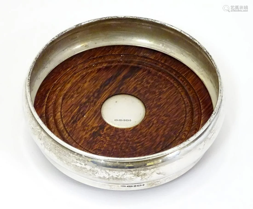 A silver wine / bottle coaster with turned wooden …