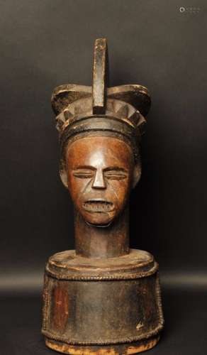 République démocratique du Congo Ethnie AMBETE Couvercle de reliquaire en bois patiné constitué d'une tête surmontée d'une coiffe. Dents en fer et barbe en cuivre. Frises circulaires en rotin. H: 61 cm x D 23 cm