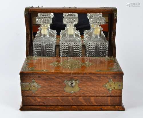 A Victorian oak and brass mounted tantalus, having three square moulded glass decanters and