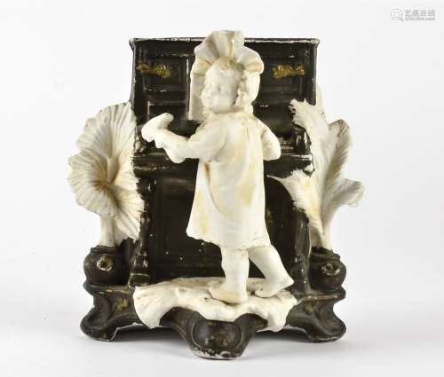 A Continental spill vase with comic subject matter, with baby, piano and hammer, height 17cm