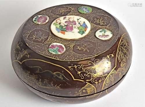 A circular lacquered container, with Chinese porcelain roundel inclusions, and a gilt enamelled