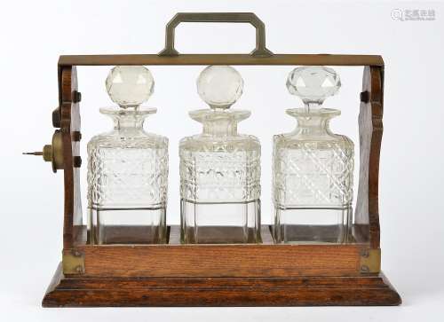 An oak framed tantalus, containing three cut glass decanters, with key