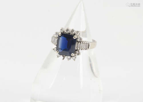 A sapphire and diamond dress ring, the step cut in four claw setting surrounded by brilliant cut and