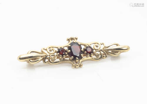 A 9ct gold garnet set bar brooch, the central oval mixed cut in claw setting flanked by two round