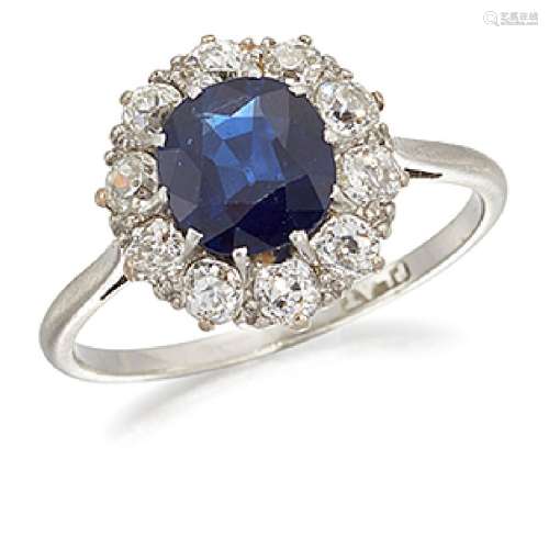 A platinum, sapphire and diamond cluster ring, the cushion shaped sapphire, weighing approximately