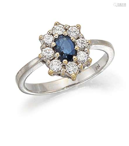 A sapphire and diamond cluster ring, the claw-set oval sapphire within a brilliant-cut diamond