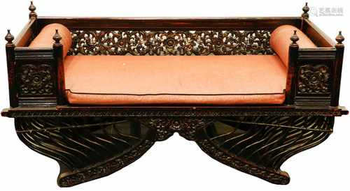 A black laquered elaboratly carved bench with roll cushions. China, second half 20th century.