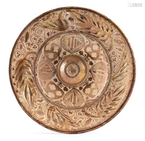 Large Hispano-Moorish navel plate. Valencia, Manises, 17th century. D. 43 cm. Sand-coloured body, with a light pink glaze and copper-coloured lustre decoration. Wide flag with notched ear decoration, flattened central projection in the middle of the mirror. Surface filled with dense vegetal ornamentation. On the edge of the l. rest, signs of age. Provenance: From a North German private collection.