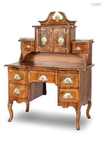 Essay desk. Dresden baroque style, second half of the 19th century. 150x110x68 cm. Exemptable. Lower section with five drawers and writing drawer, top with two doors and two drawers. Blasted pediment. Rich brass ornaments. Nine painted porcelain plaques. Rest. Age-sp. walnut, walnut burl and other putto marquetry on the writing tablet. Provenance: Collection of a Southern German entrepreneur.