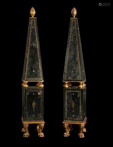 Pair of large obelisks. Classicist style. H. 207 cm. Two-piece construction. Partly carved and gilded. Mirror trimming, reverse partly gilt and engraved, thus in a kind of Verre Eglomise technique. Rest. Aged. Paw feet and pine cones as a tip.