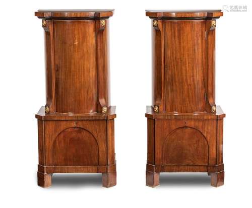 Pair of Empire pillar cupboards. North German, circa 1820. 115x53x31 cm. Each with one door, underneath drawer. Trimming with gilded lion heads. Rest. Aged mahogany, partly ebonized. A carefully crafted pair of ornamental half cabinets with cylindrically shaped tops in typical provenance design and in an attractive state of preservation.