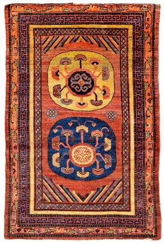 Ancient Khotan. East Turkestan, first half of the 19th century 169 x 111 cm. Beautiful Khotan with two disc medallions filling the stock, which alternately cover the tomato red ground in ink blue and yellow. Stylized floral motifs and hooked core motifs belong to the classic pattern canon of knotting from the Tarim Basin. Alternating stripe motifs border the background at the lower and upper edge. Among the borders of the enclosing frame a stylised meander border and a geometric floral tendril. Antique collector's item. Edge damage, one edge minim. incomplete. Flor part. thin. Part. Re-knotting.