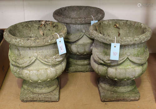 A set of three 20th century cast composition stone garden urns, the half-reeded bodies with swag