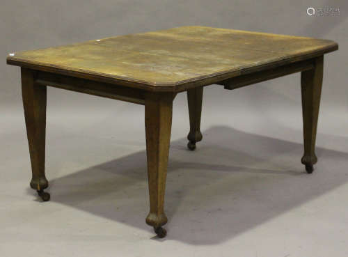 An Edwardian oak extending dining table with single extra leaf, raised on square tapering block