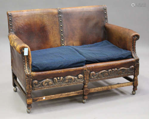 An early 20th century Jacobean Revival oak and brown leather two-seat settee with carved and brass