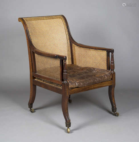 A Regency mahogany framed library armchair with caned seat and back, fitted with a brown leather