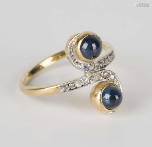 A gold, cabochon sapphire and diamond twin cluster ring in a scrolling crossover design, mounted