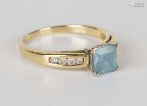A gold, pale blue gem and diamond ring, claw set with the square step cut blue stone between diamond