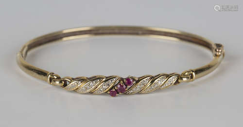 A 9ct gold, ruby and diamond oval hinged bangle, claw set with a row of three circular cut rubies