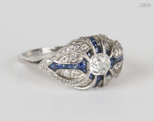A white gold, diamond and sapphire ring in a scrolling oval form, claw set with the principal oval