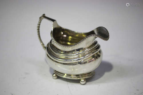 A George III silver cream jug of cushion form with gadrooned rim and beaded handle, raised on ball