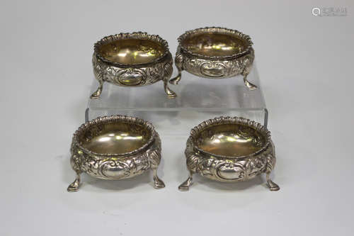 A harlequin set of four Victorian silver circular salts, each embossed and engraved with foliage,