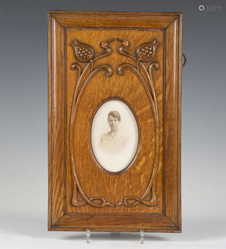 An Edwardian Arts and Crafts oak photograph frame, the oval aperture within a surround of two