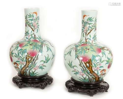 China, Republic period (1912-1949)Pair of large polychrome porcelain tianqiuping vases, with nine peaches of longevity, also decorated in mirror with flowering branches and bats in flight Apocryphal Qianlongmark in blue under coverH: +/- 55 cm (excluding carved wooden bases)
