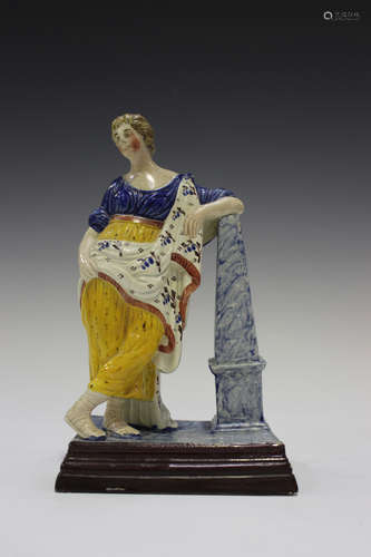 A Prattware figure of a classical lady leaning on an obelisk, circa 1800, raised on a stepped