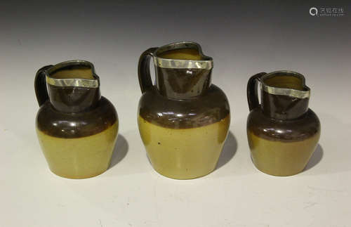 Three graduated salt glazed stoneware jugs, late 19th century, each mounted with a silver rim,