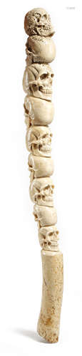 A FOSSILISED WALRUS OOSIK BONE carved with nine human skulls and with a handgrip 49cm long