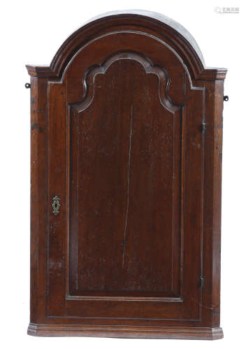 A GEORGE II OAK HANGING CORNER CUPBOARD the arched top above a shaped fielded panel door,