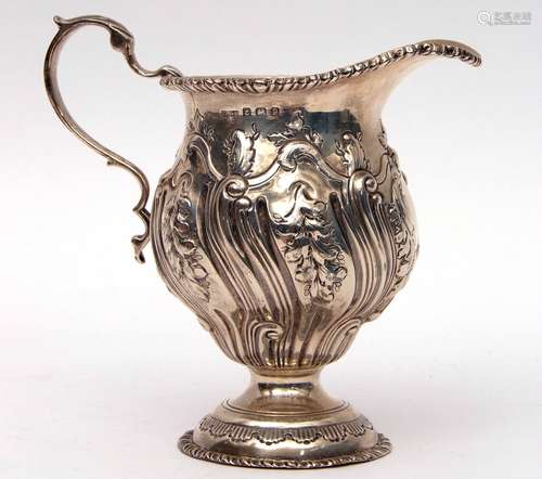 George V cream jug of circular baluster form in George II style, heavily chased and embossed with