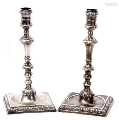 Pair of George II candlesticks with multi-knopped stems to dished square bases with gadrooned edges,