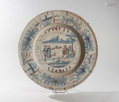 NEVERS?Round dish with blue and manganese decorationin the middle of two couplesin a landscape and on the wing ofstylized flowers.18th century.Diameter : 49 cmCooking defects and cracks