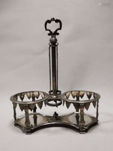 Silver oil and vinegar maker. Foreign work, 18th century. The circular flask mounts are fixed to the edge of the plate cut with filleted sides, by the uprights in the form of curved columns with a gadrooned base. The upper edge of the amati mounts, engraved with fleurons and volutes, is underlined by a frieze of lambels engraved with fleurons on an amati background. Decorated with a radiating motif and button in the centre of the tray. Central stem with sides ending in a scrolled grip and matching two chains. Two flasks with stoppers, one of which has several restored breaks.Top. (stem): 22.7 cm; Net weight: 402 g.