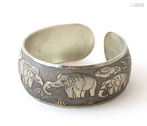 An Art Deco white metal bangle formed bracelet with elephant decoration .