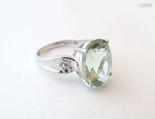 A 9ct white gold ring set with a pale green stone, possibly a paraiba, flanked by diamonds.