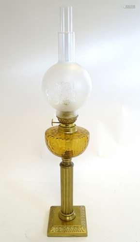 An oil lamp with brass square base supporting a column stand and dimpled orange glass reservoir.