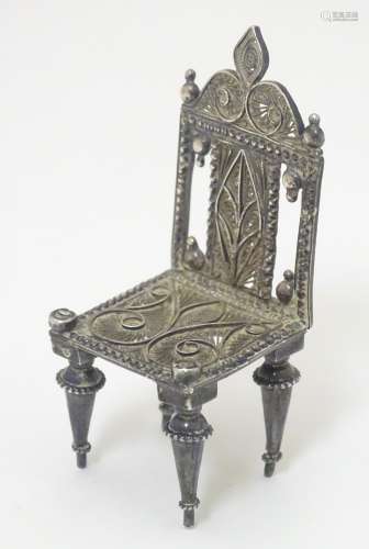 A silver miniature model of a chair with filigree decoration.