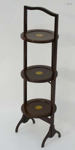 An early 20thC mahogany folding cake stand with three marquetry decorated tiers.