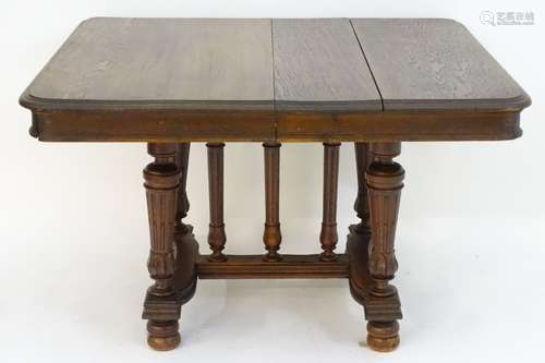 A 20thC oak dining table standing on fluted tapering supports and having central turned columns