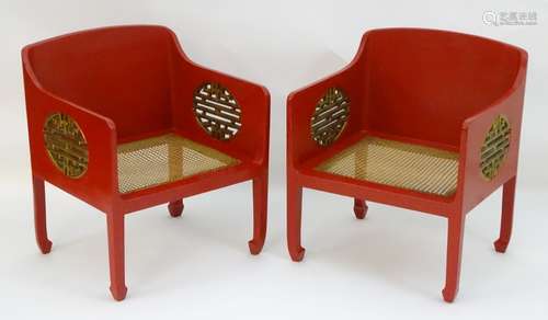 A pair of Chinese style red painted armchairs with pierced gilt painted sides and caned seats.