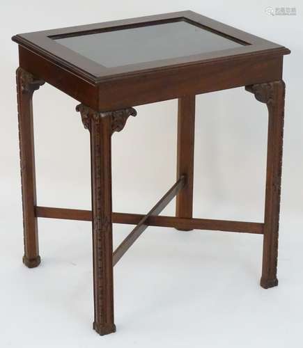 A mahogany bijouterie table with a glass top, carved earpieces and legs united by a cross stretcher.