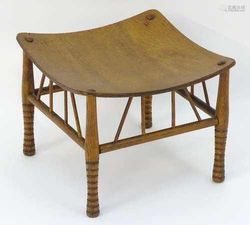 An early 20thC oak Liberty style Thebes stool with a concave seat above brace supports and turned