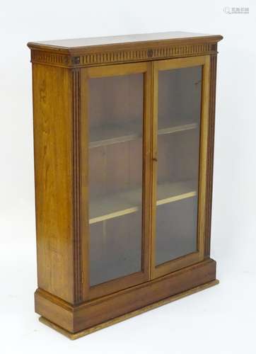 An early 20thC glazed oak bookcase with a fluted frieze and carved floral motifs above two glazed